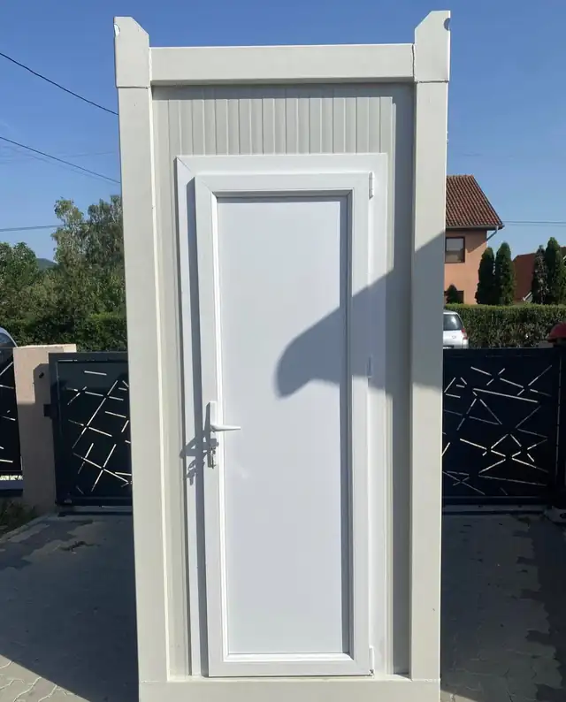White deluxe restroom cabin with a panel door, set outdoors