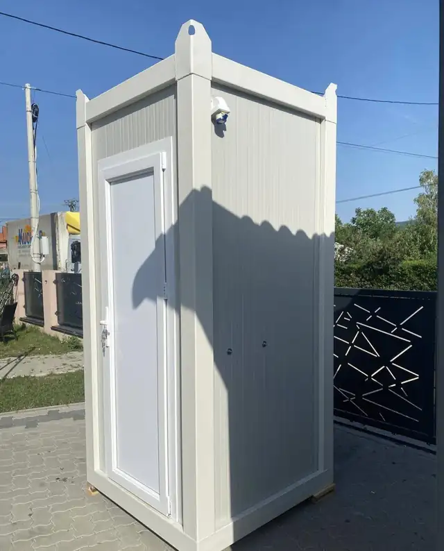 White deluxe restroom cabin standing on paving beside a fence