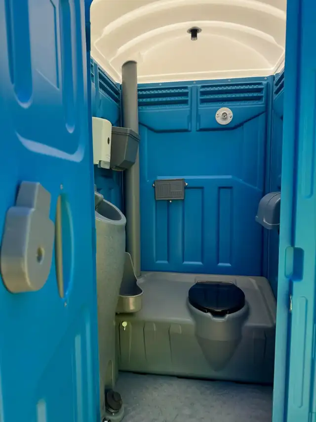 Inside a standard porta potty showing the seat, urinal and walls
