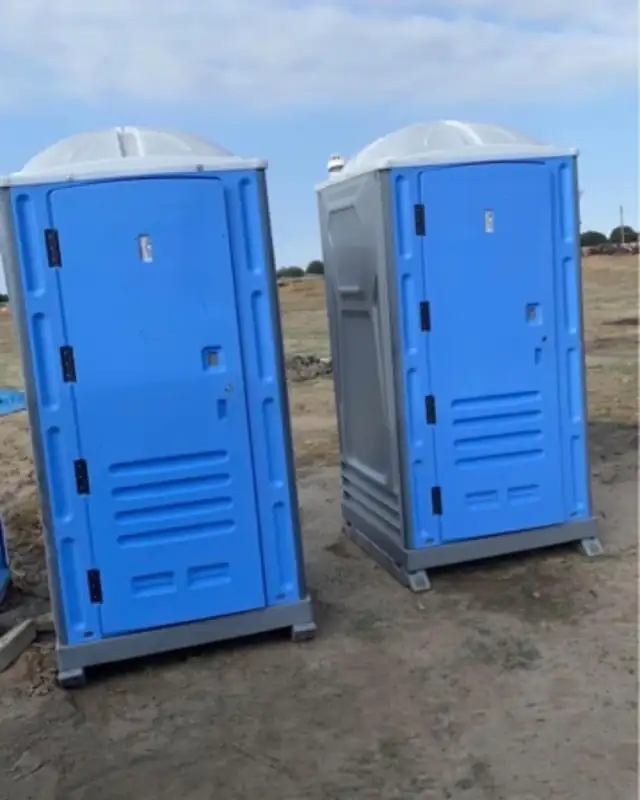 Two blue standard porta potties set side by side on gravel, ready for renters